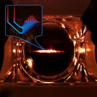 Glowing elongated cloud of cold atoms inside a vacuum chamber, with an inset graph of the stored light